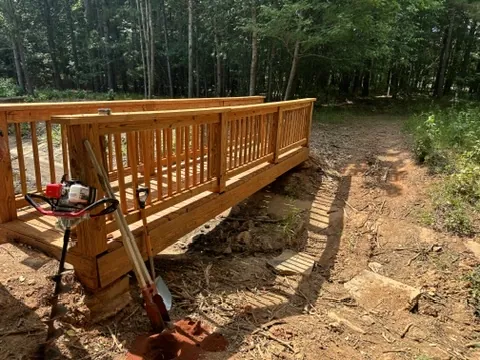 A newly built wooden footbridge on a woodland trail with a post-hole auger and digger beside it